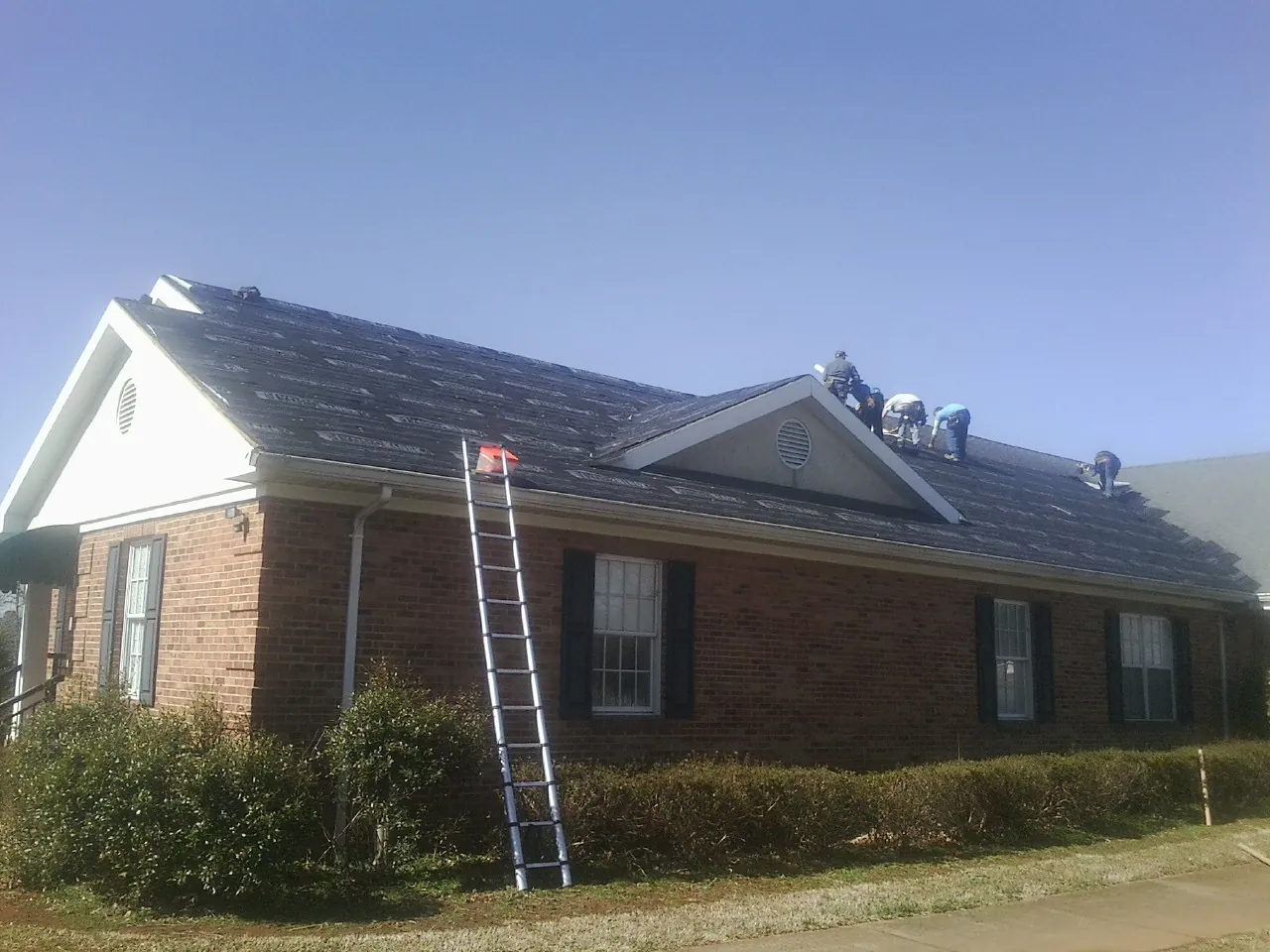 Crew tearing shingles off a brick ranch roof with a ladder set — Emergency Roof Repair work by our crew in Brookshire
