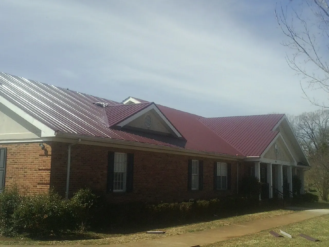 Red metal roof with gabled entries on a long brick building, from a Hail Damage Roof Repair job in Brookshire
