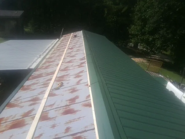 Old rusted panels beside newly installed green metal roofing — Wind Damage Roof Repair by Roofing Brothers in Brookshire
