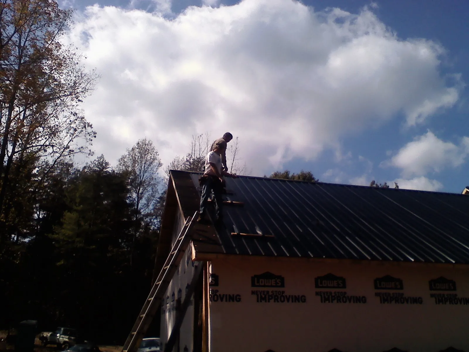 Roofer fastening dark metal panels high against a cloudy sky, from a Roof Inspection job in Brookshire